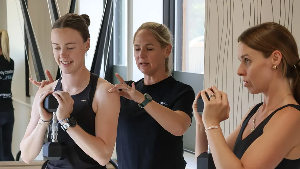 A Tomorrow coach guiding two clients through a strength exercise