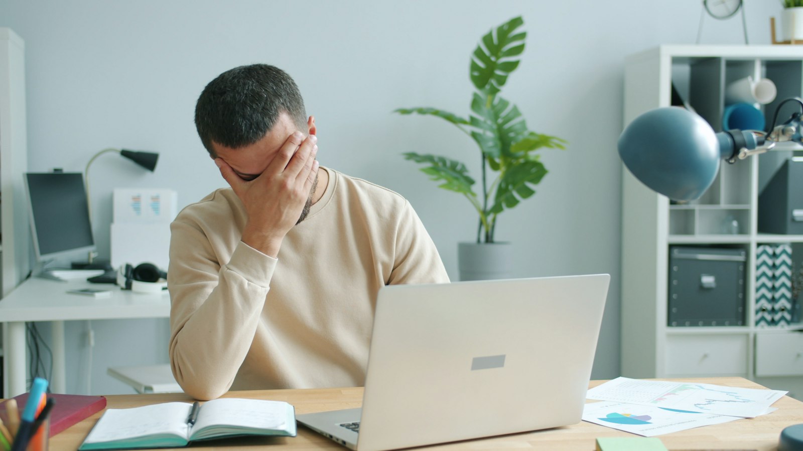 A stressed man at his desk rubbing his face in front of a laptop